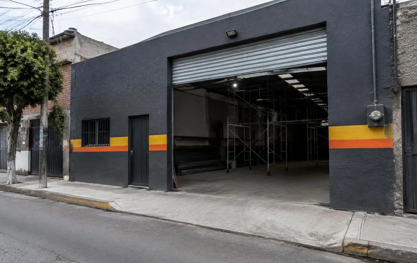 Fachada de bodega gris oscuro con franja amarilla y naranja y cortina abierta (imagen ilustrativa)